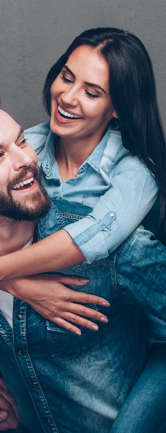 Man holding a woman on his back while they smile at each other